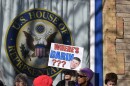 A group of protestors stand in front of a window with the U.S. House of Representatives logo on the window. A woman holds up a sign that says, "Where's Darin?" and a picture of Rep. Darin LaHood.