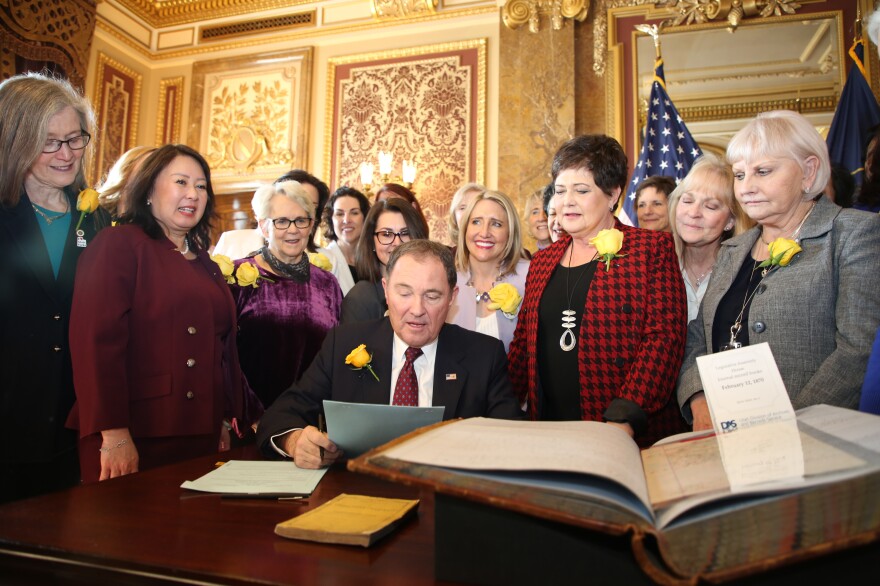Utah Gov. Gary Herbert signs bill honoring the state's pioneering women suffragists on Wednesday. He's surrounded by state senators and representatives, and his wife, who are all wearing the yellow rose symbolizing suffrage.<em> </em>
