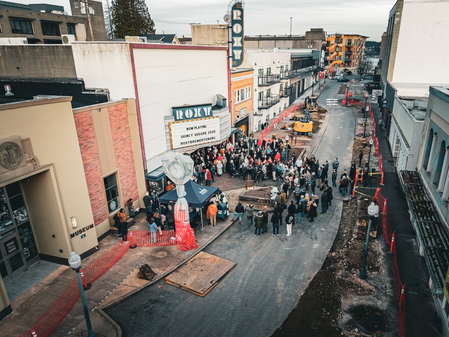 A crowd stands in front of a theater with a marquee on a street partially under construction