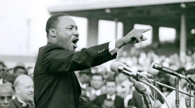 Black and white photo of a man speaking in front of microphones to a crowd
