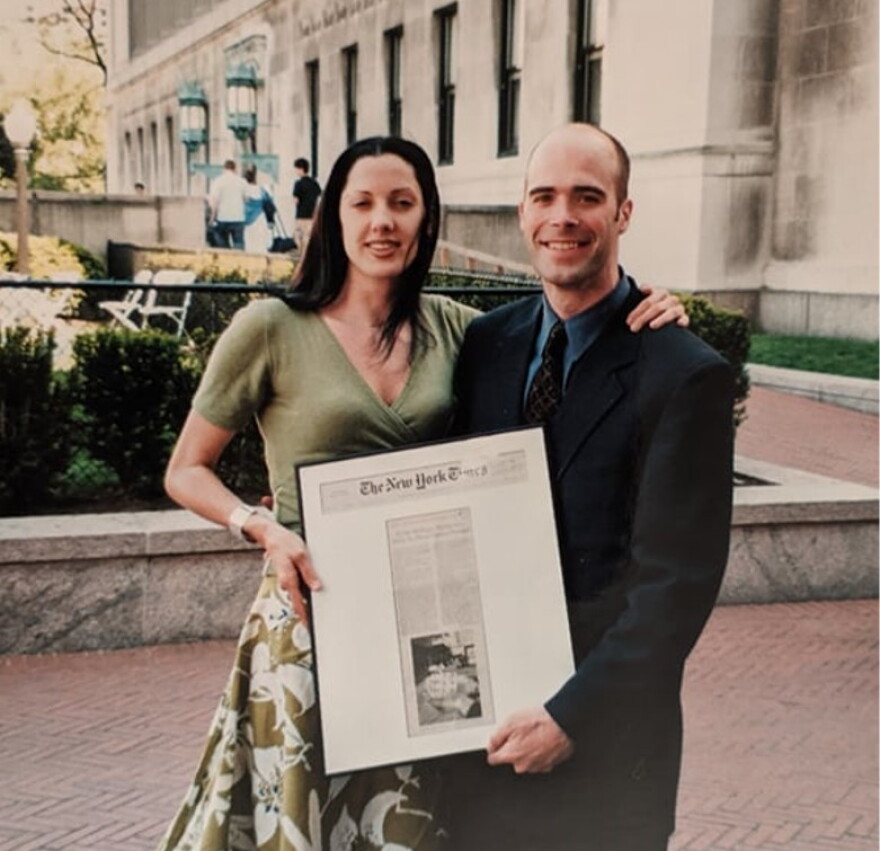 A man and a woman hold a framed picture of a New York Times article they reported and wrote in 2002.