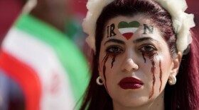 A woman stands on the tribune with her face painted in memory of Mahsa Amini, a woman who died while in police custody in Iran at the age of 22, prior to the World Cup group B soccer match between Wales and Iran, at the Ahmad Bin Ali Stadium in Al Rayyan , Qatar, Friday, Nov. 25, 2022. (Frank Augstein/AP)