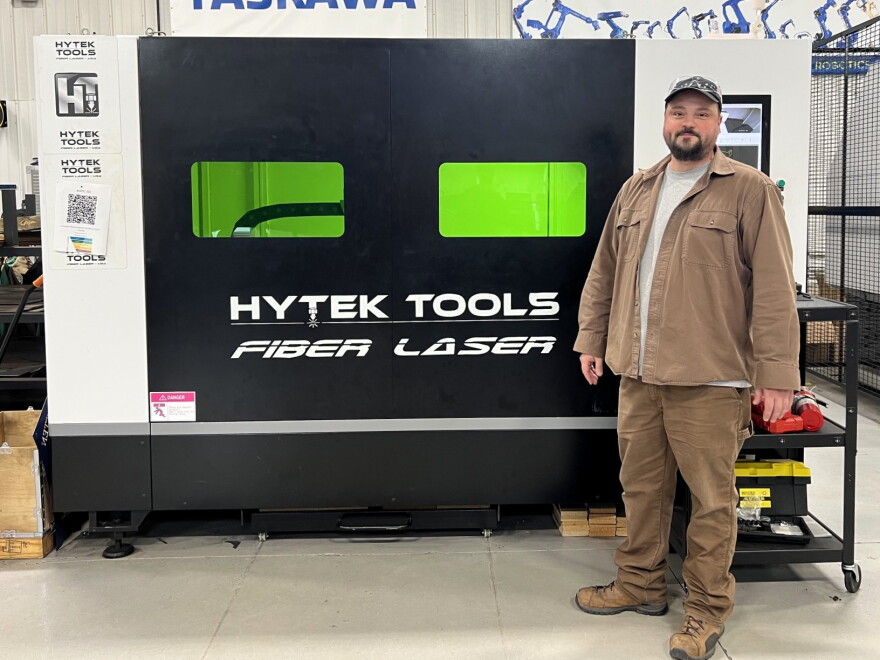 A man stands near a piece of high tech manufacturing equipment.