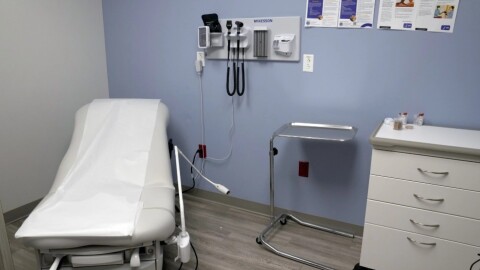 The inside of an medical exam room with a bed on the left and cabinet on the right