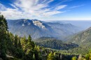 A sprawling mountainous landscape covered in green trees. The sky is partly cloudy.