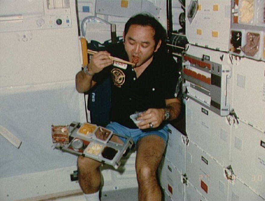 Mission specialist Ellison S. Onizuka takes a meal break on the mid-deck of the Discovery space shuttle during the STS 51-C mission in the 1980s.