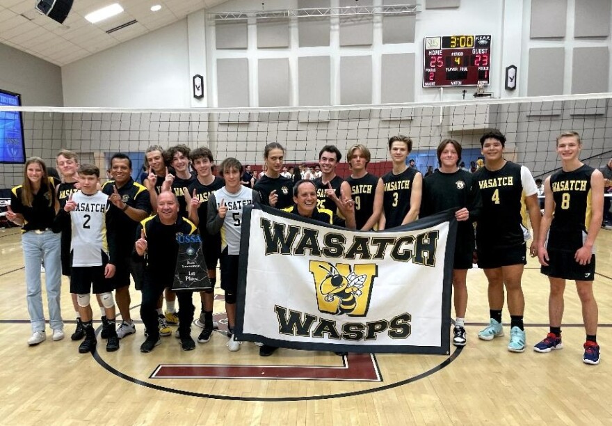 Head Coach Duke Mossman holds the state championship trophy with his team standing behind him at the Layton Christian Academy gym Saturday after the title game.