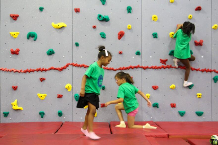 Children scale a climbing wall and cartwheel across mats during a summer camp at a recreation center in Baton Rouge on June 2, 2026.