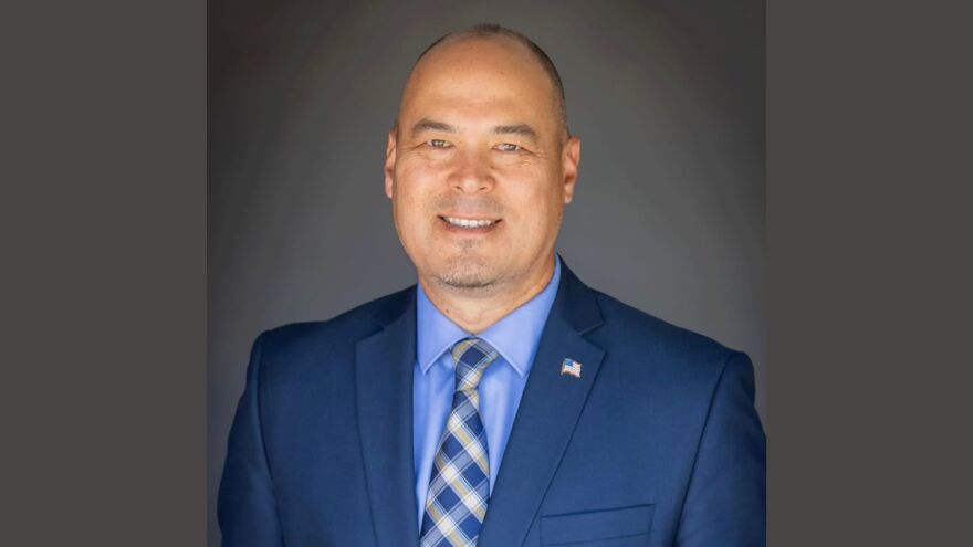 An official portrait of Nampa Mayor Rock Hogaboam. He is smiling, looking at the camera. He is wearing a blue suit, with a small American flag pinned onto it.  