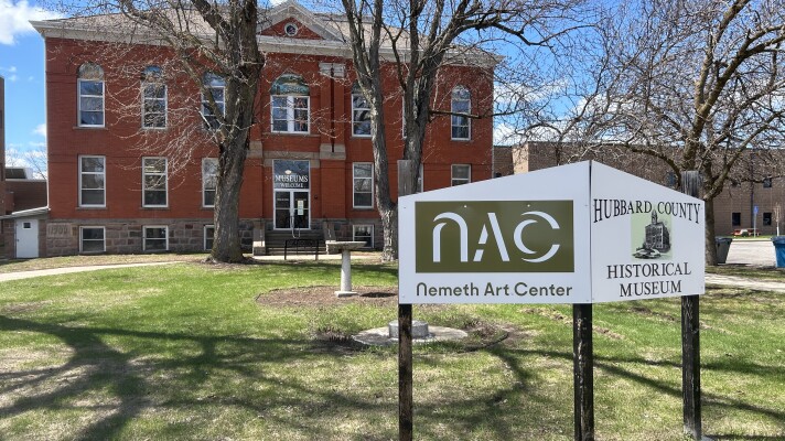 A sign in front of an old brick building surrounded by trees and green grass.