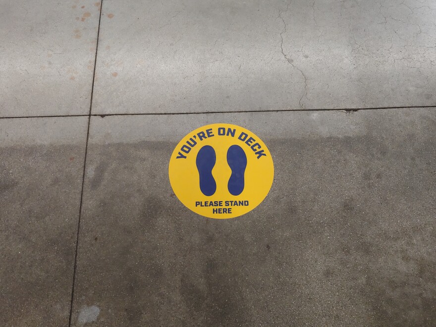 A floor sign for the second person in line at a concession stand.