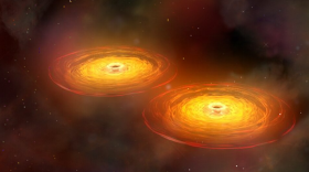 This illustration shows a stage in the merger of two galaxies that forms a single galaxy with two centrally located supermassive black holes surrounded by disks of hot gas. The black holes orbit each other for hundreds of millions of years before they merge to form a single supermassive black hole that sends out intense gravitational waves.