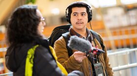 A NPR Network Reporter interviews a subject matter inside a brightly lit building. 