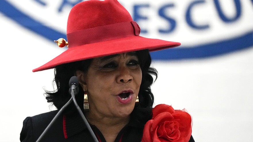 head shot of African American woman in a red brimmed hat waring a rose on her shoulder 