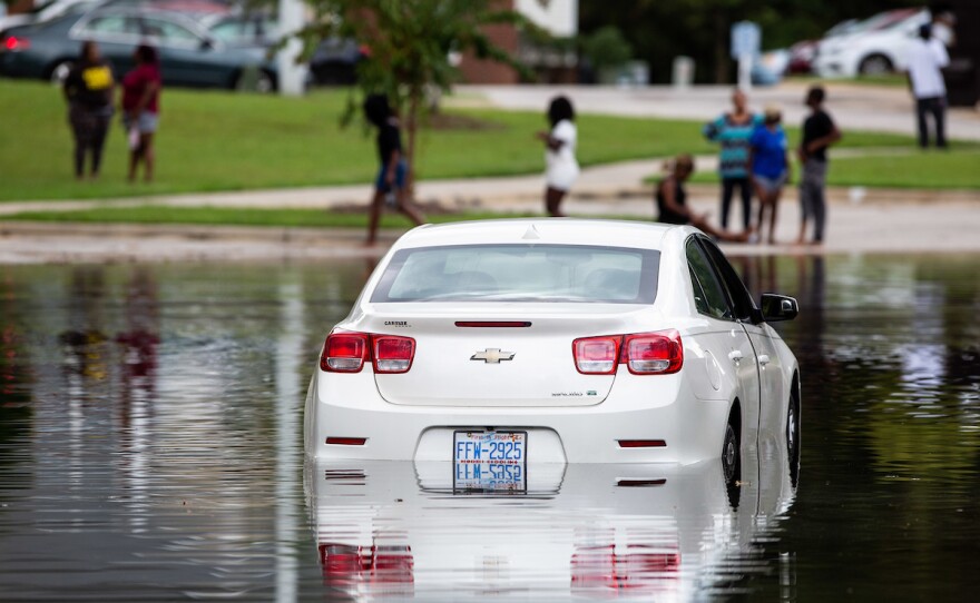 Residents of an apartment complex in Fayetteville, look at a flooded car in a parking lot on Tuesday, Sep. 18, 2018.