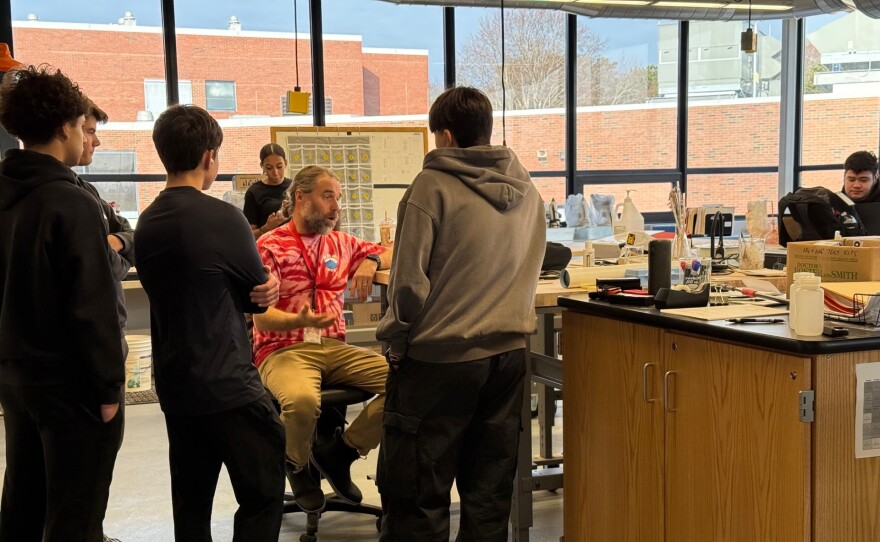 Students standing around a teacher who is seated at the front of a science lab