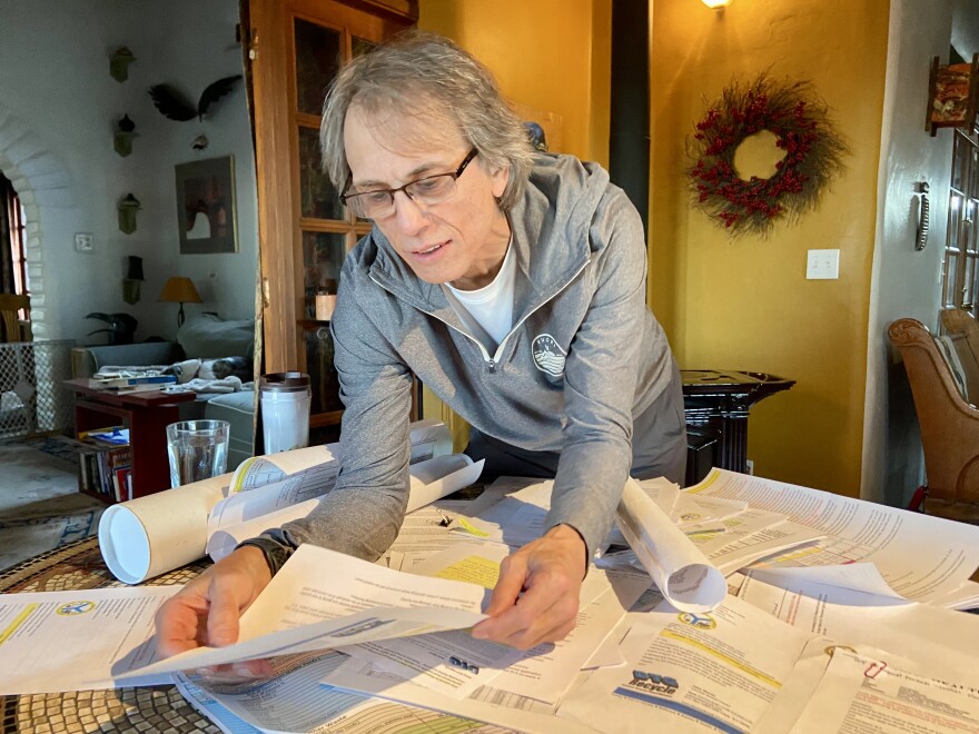 A man in a gray shirt examines documents on a kitchen table.