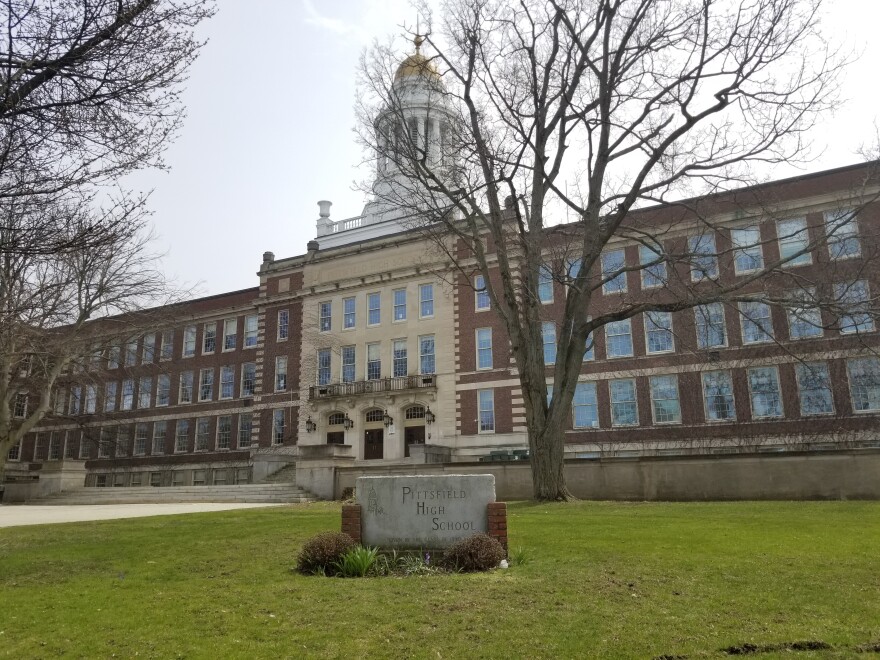 A long brick building sits beyond a green lawn and trees with a rotunda with a gold spire rising above it