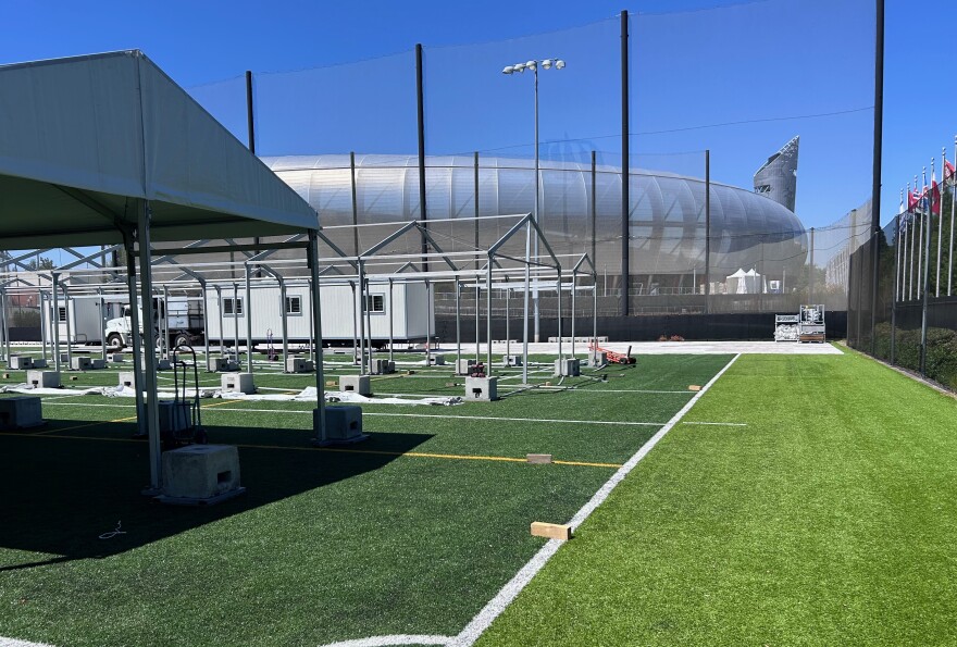 Tents being erected on a turf field with a stadium behind