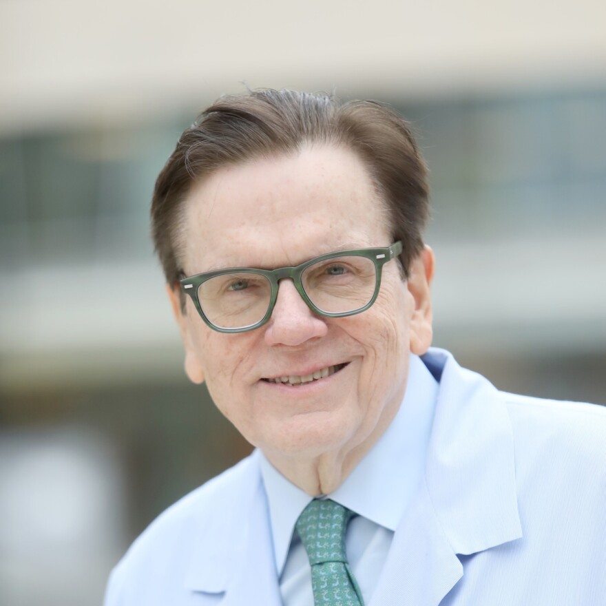 A man with brown hair and green eyeglasses stands smiling at the camera for a headshot. 
