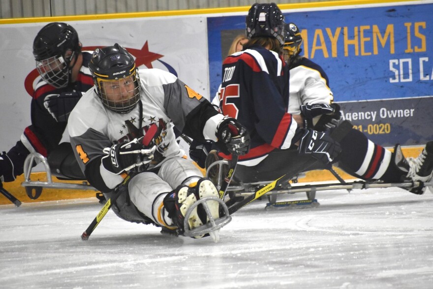 Matt Daniels, wearing a white hockey uniform, propels himself on a sled hockey sled. 