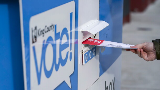 A person puts their ballot in a drop box.