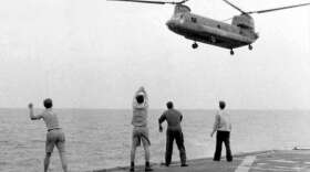 Aboard	the	USS	Kirk,	crew	members	signal	the	Chinook	to	hover	over	the	deck	and	drop	its	passengers	out.April	29,	1975. Photo courtesy of Hugh	Doyle