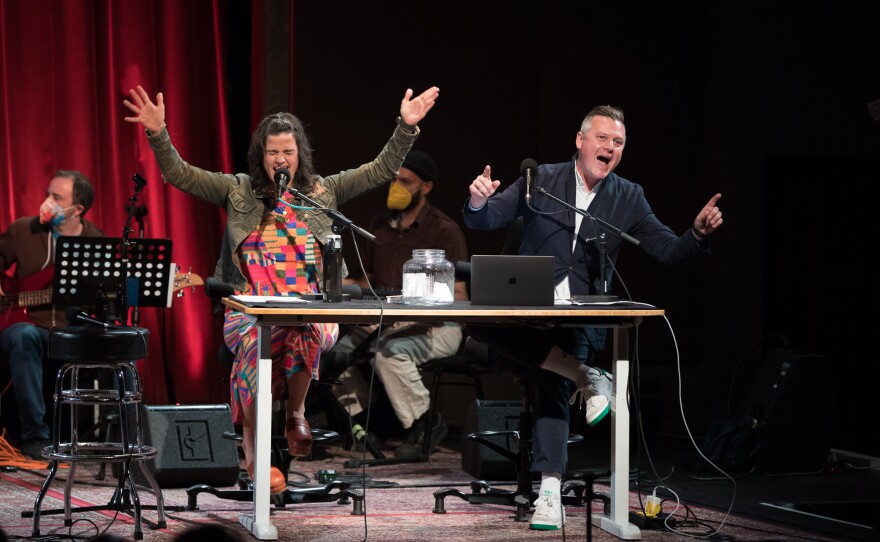 Two podcast hosts on the stage in front of their microphones. 