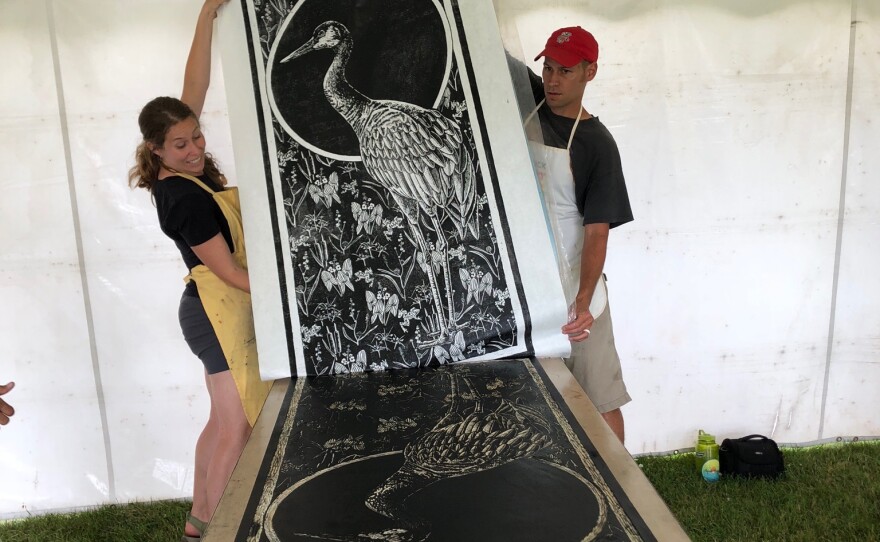 Rebecca Jabs (left) and Anthony Bauer (right) lifting a woodcut print of a Sandhill Crane at the 2018 street roller festival, Really Big Prints.