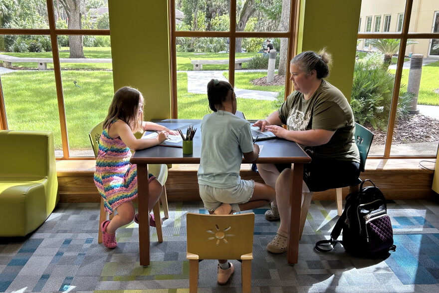 Cheryl Dawson (right), a nurse care coordinator for Partnership for Strong Families, joins a virtual meeting as her daughters, Aria, 8 (left), and Renny, 7, color at the Hawthorne branch of the Alachua County Library District. (Molly Seghi/WUFT News)