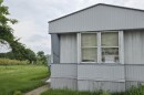 A mobile home sits in a green field with a "for sale" sign in its window.