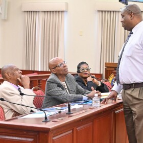 Pictured: Senator Kenneth Gittens, standing, speaks with VIPA board members during a Committee on Rules and Judiciary hearing at the Earle B. Ottley Legislative Hall. Seated from left to right are Celestino White Sr., Willard John, and Leona Smith.