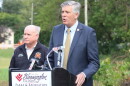 Darin LaHood speaks at the Bloomington Parks & Recreation podium as Mayor Dan Brady stands behind him in his fire department jacket.