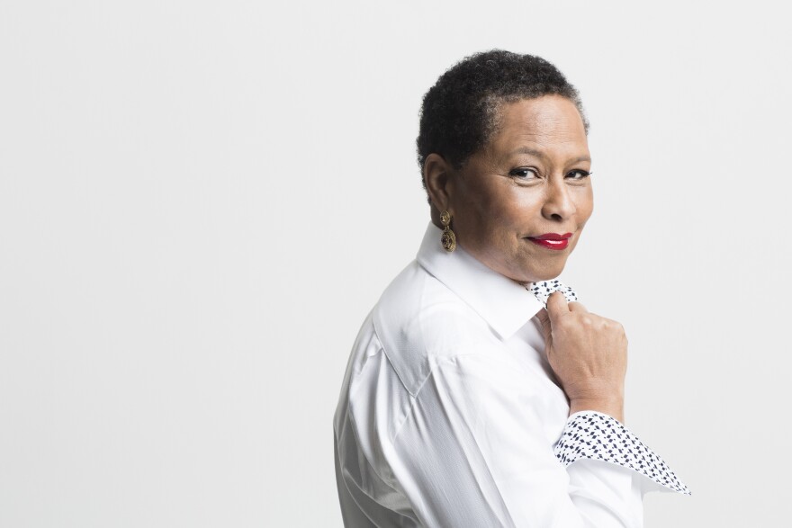 A woman with short hair and wearing a white button up shirt soft smiles at the camera.