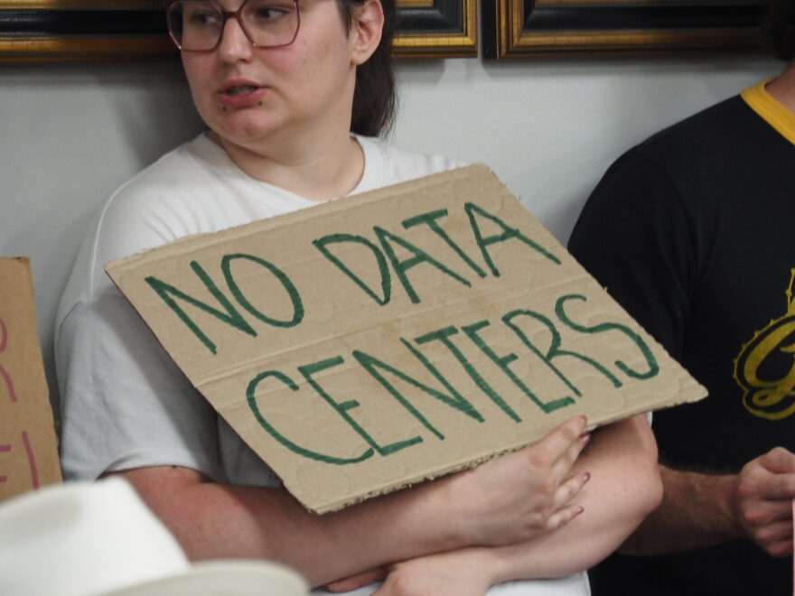 An audience member attending a Pulaski County Quorum Court agenda-setting meeting holds a sign opposing data centers on June 9, 2026.