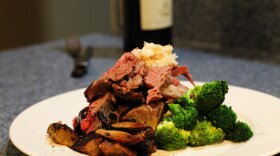 Beef prime rib dinner plate, with demi glace, broccoli, horse radish and a bottle of wine in background. Michael J. Bennett, CC BY-SA 3.0 <https://creativecommons.org/licenses/by-sa/3.0>, via Wikimedia Commons
