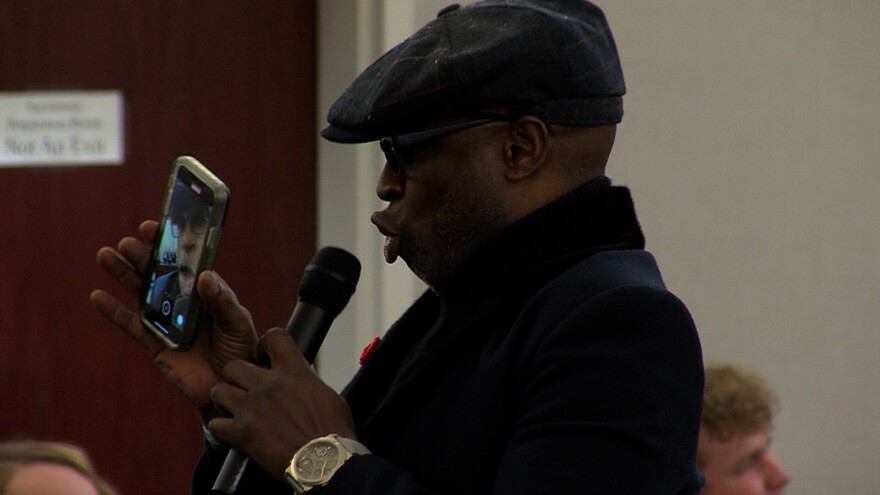 Alex Boyé singing into a microphone while filming himself on a cell phone. 