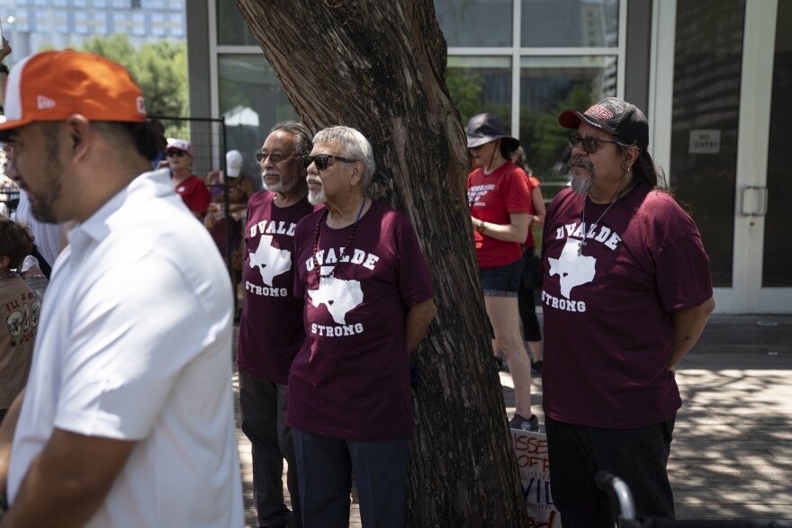 Men with t-shirts reading "Uvalde strong," in honor of the school shooting, attend a protest outside.