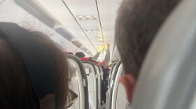 A passenger holds an IV saline bag above the aisle as medical volunteers respond to an in-flight emergency aboard a flight approaching Ben Gurion Airport near Tel Aviv, Israel, on October 17, 2026. The aircraft encountered turbulence as passengers and crew worked to stabilize a woman experiencing difficulty breathing.
