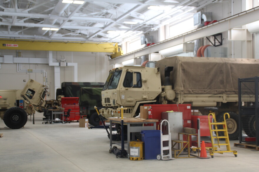 Military vehicles are parked for servicing inside of a National Guard field maintenance shop.