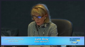 Hillsborough School Board Chair Lynn Gray wears glasses and speaks into a microphone at a school board meeting