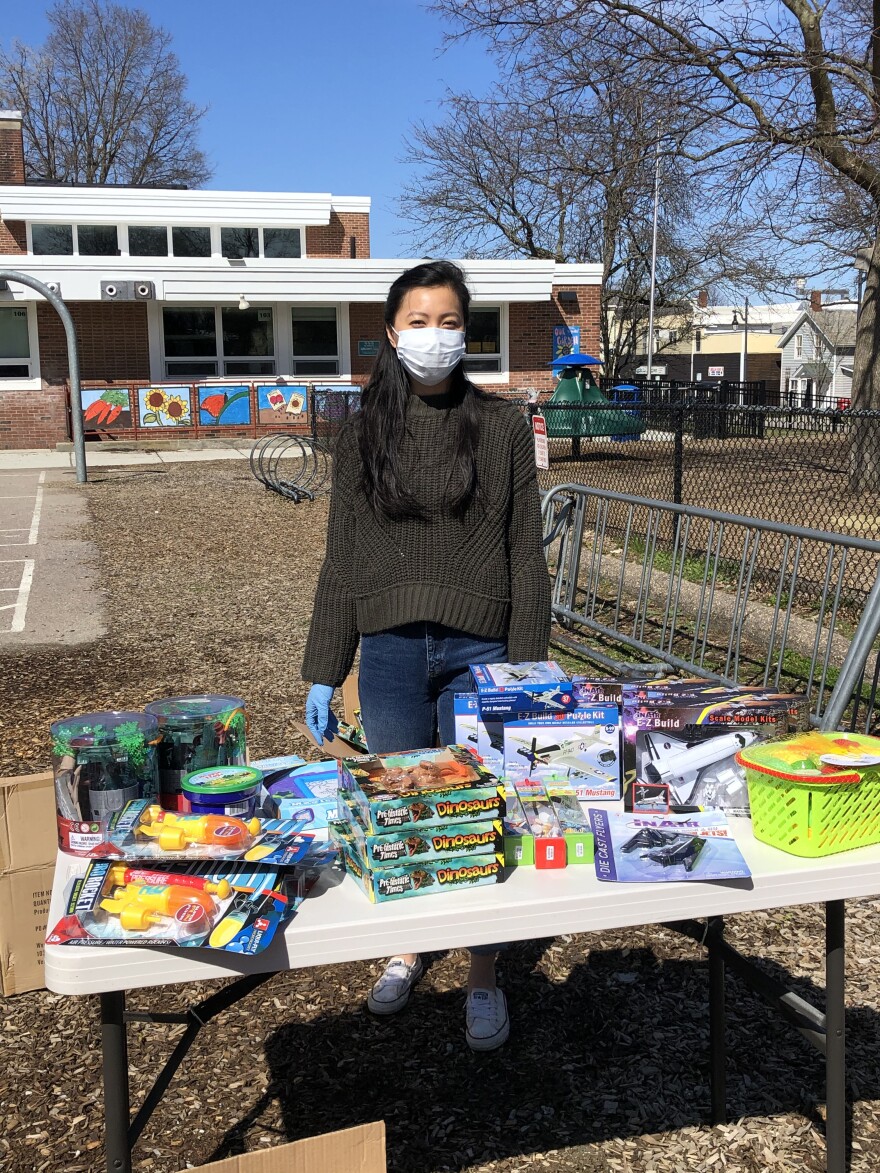 A person in a face mask stands behind a table with toys on it.