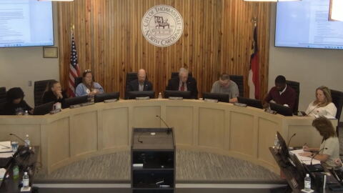 a group of people sitting at a meeting, a sign reading "City of Thomasville North Carolina" 