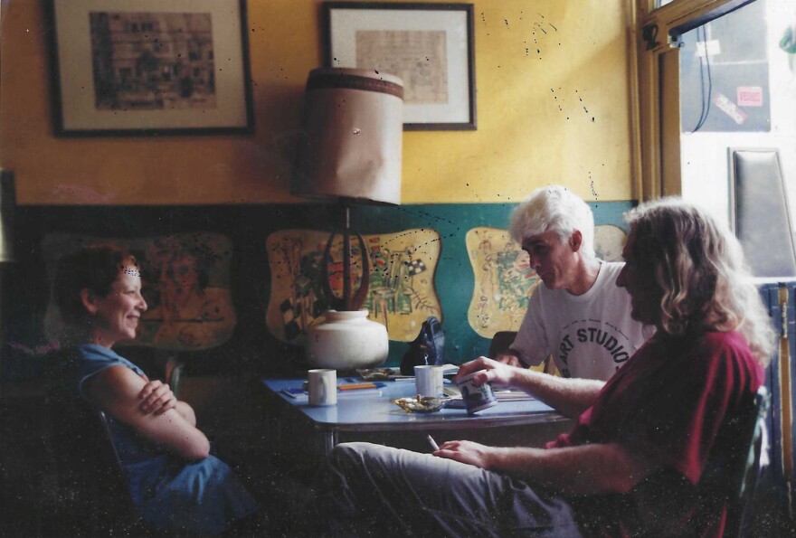 Two men and a woman sit around a table while drinking coffee and talking.