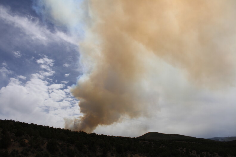 Wildfire smoke rises above a hillside