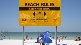 A yellow beach sign encourages people to stay six feet apart.