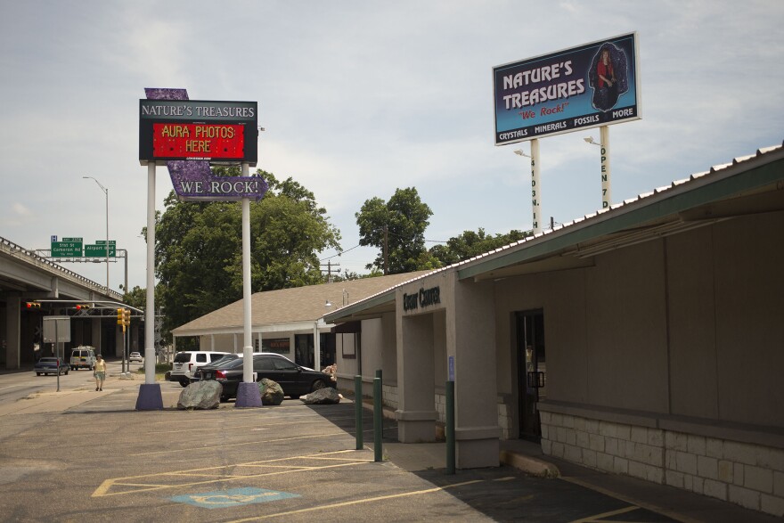 Exterior shot of the business. On the left are the upper decks of I-35. In the middle of the image is the parking lot. On the right is Nature's Treasures. Behind the business towers a large billboard that says, "Nature's Treasures. We Rock! Crystals, minerals, fossils and more."