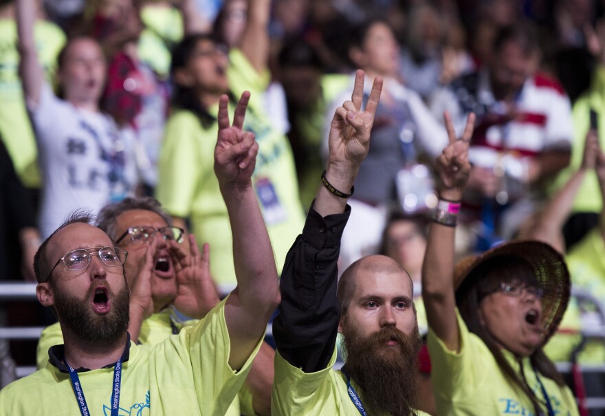 Yellow-shirted Bernie Sanders delegates shout anti-war slogans and hold up peace signs on the convention floor.