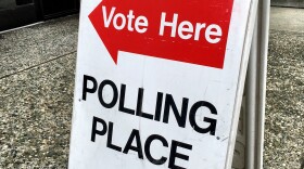 A red arrow with the text 'vote here' and black letters saying 'polling place' are posted on a white fold out sign.