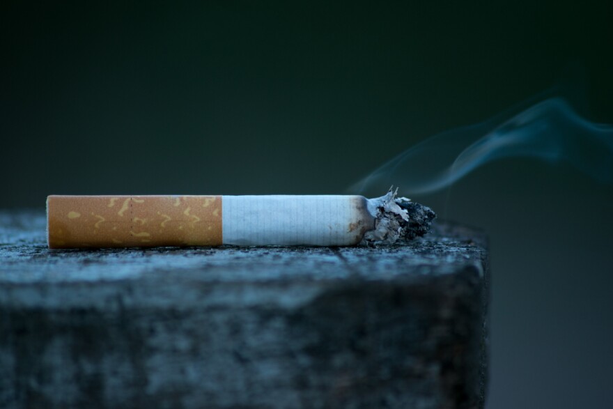 A cigarette with smoke billowing laying on a stone.